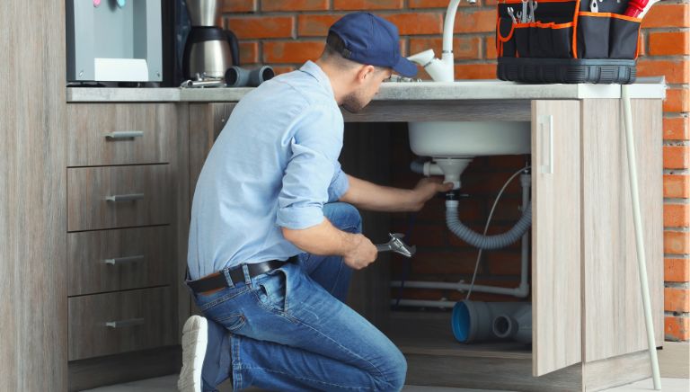 A plumber is repairing under the sink
