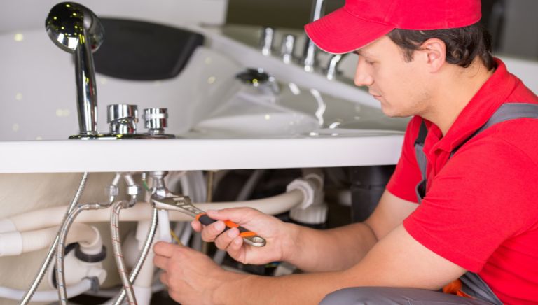 A plumber is repairing under the sink